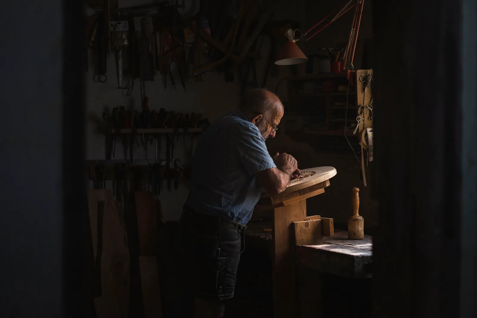 Officina in penombra, un uomo al banco sotto la luce di una lampada
